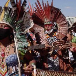 Indigenous Musicians wearing colorful headdresses made of feathers and colorful clothing, playing guitars