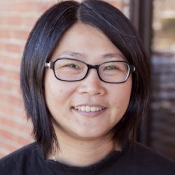 outdoors headshoot of Christina Chia, brick wall & glass door in the backgrouond