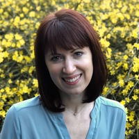 Headshot of Julie Nelson, outdoors with yellow flowering shrub in background