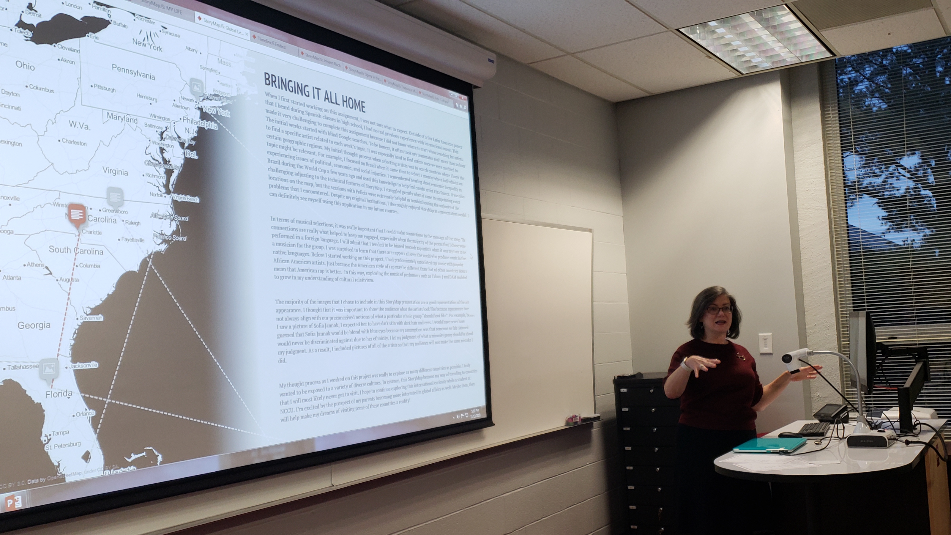 interior photo of woman (right) presenting powerpoint on screen (left 2/3)